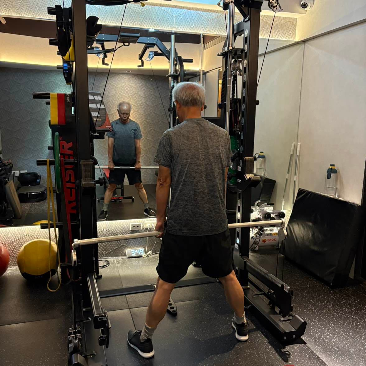 張立秋在鏡前 Keiser 訓練架內雙手持槓，鏡中可見正面。