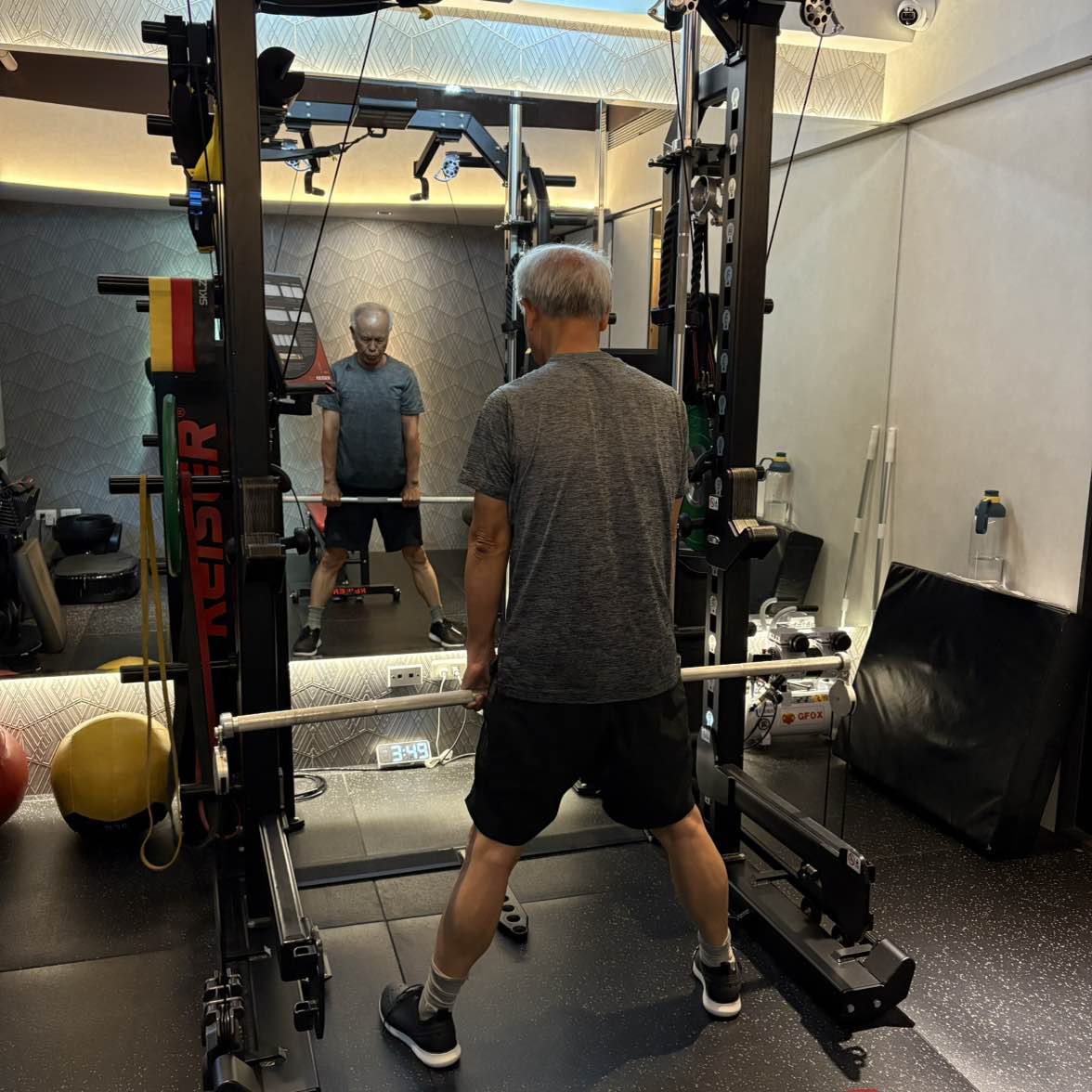 張立秋在鏡前 Keiser 訓練架內雙手持槓，鏡中可見正面。